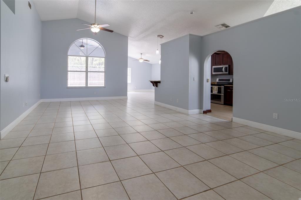 A spacious living area with light blue walls, tiled floors, and an arched kitchen entryway — 1352 WOODFIELD OAKS DRIVE, APOPKA, FL