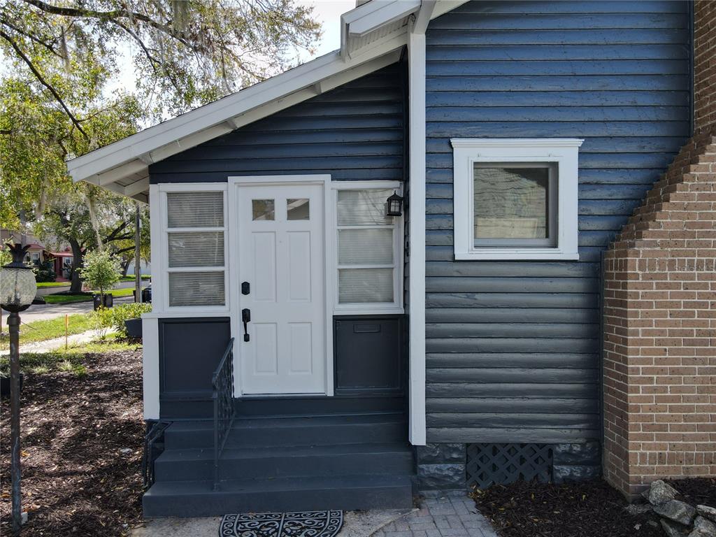 A blue-sided house exterior features a white front door, side windows, and brick accents — 16 N LAWSONA BOULEVARD, ORLANDO, FL
