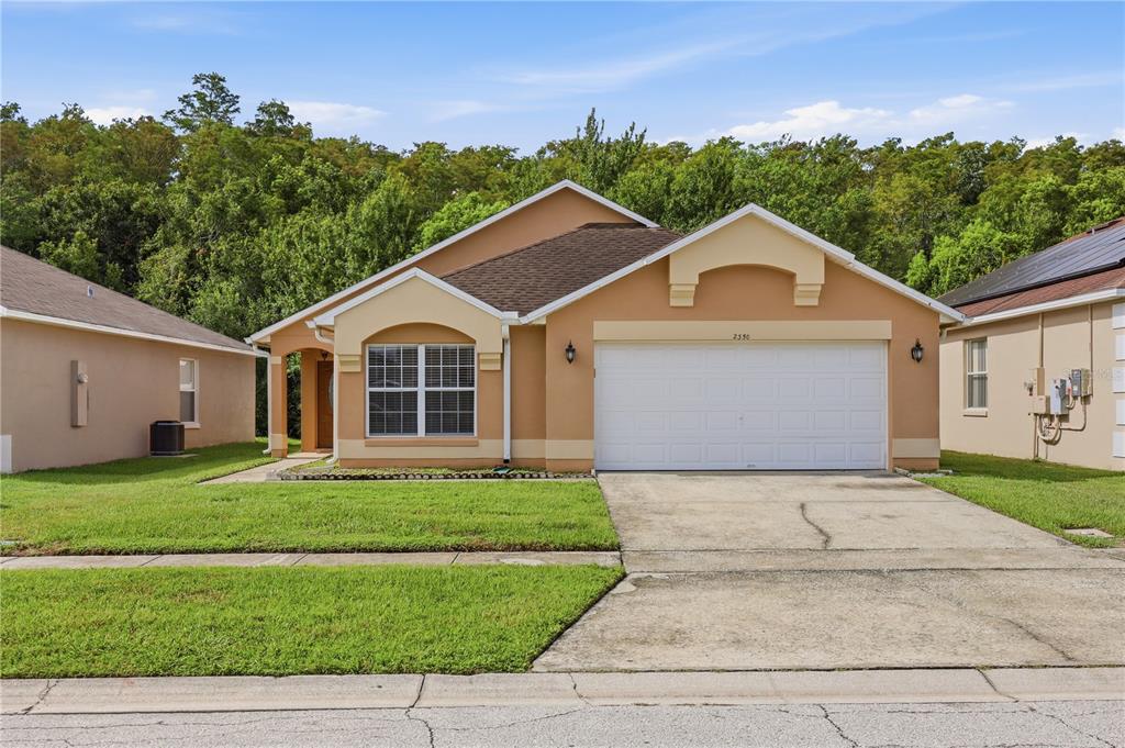 A single-story tan house with a two-car garage and a front lawn — 2350 TOPAZ TRAIL, KISSIMMEE, FL