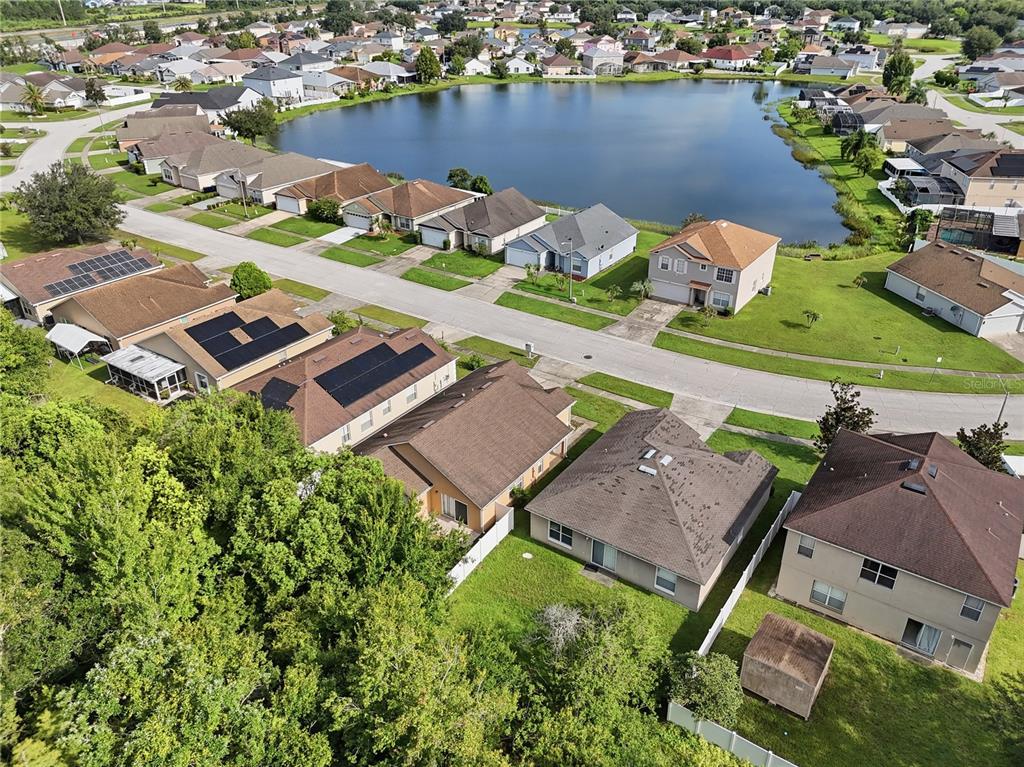 An aerial view shows a suburban neighborhood with houses, a central lake, and green lawns — 2350 TOPAZ TRAIL, KISSIMMEE, FL
