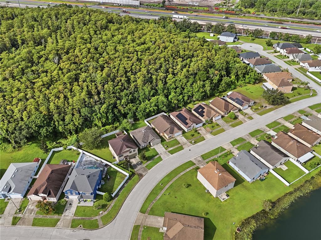 An aerial view shows a suburban neighborhood with houses, a large wooded area, and a highway — 2350 TOPAZ TRAIL, KISSIMMEE, FL