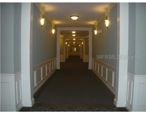 A long, carpeted indoor hallway features white wainscoting and wall-mounted light fixtures — 3368 ROBERT TRENT JONES DRIVE UNIT 40208, ORLANDO, FL