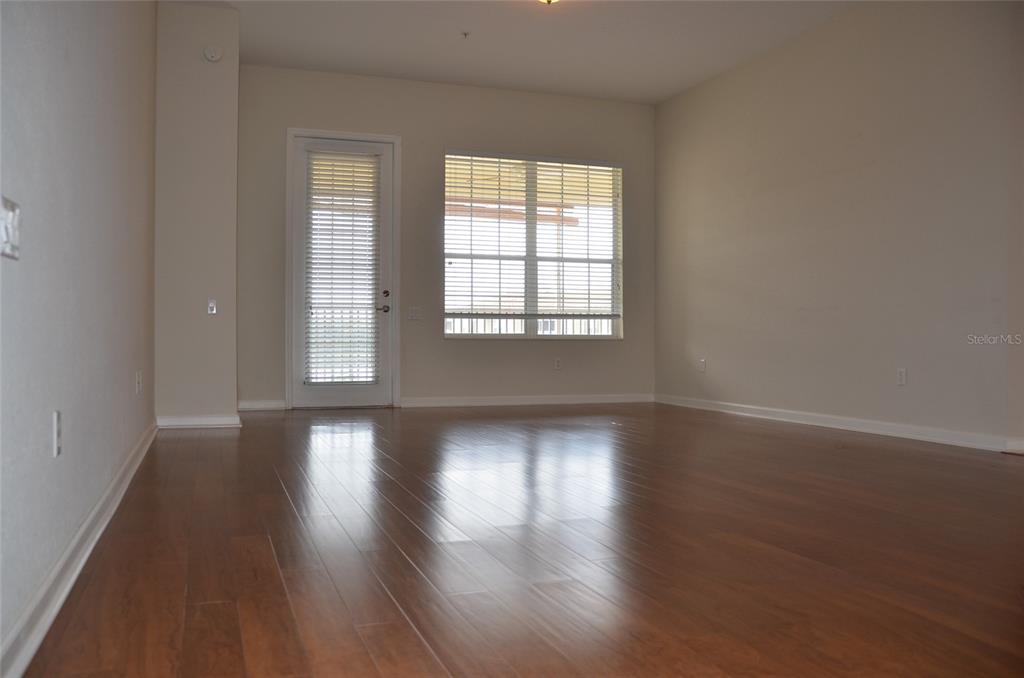 An empty room features hardwood floors, a glass-paneled door, and a large window with blinds — 3368 ROBERT TRENT JONES DRIVE UNIT 40208, ORLANDO, FL