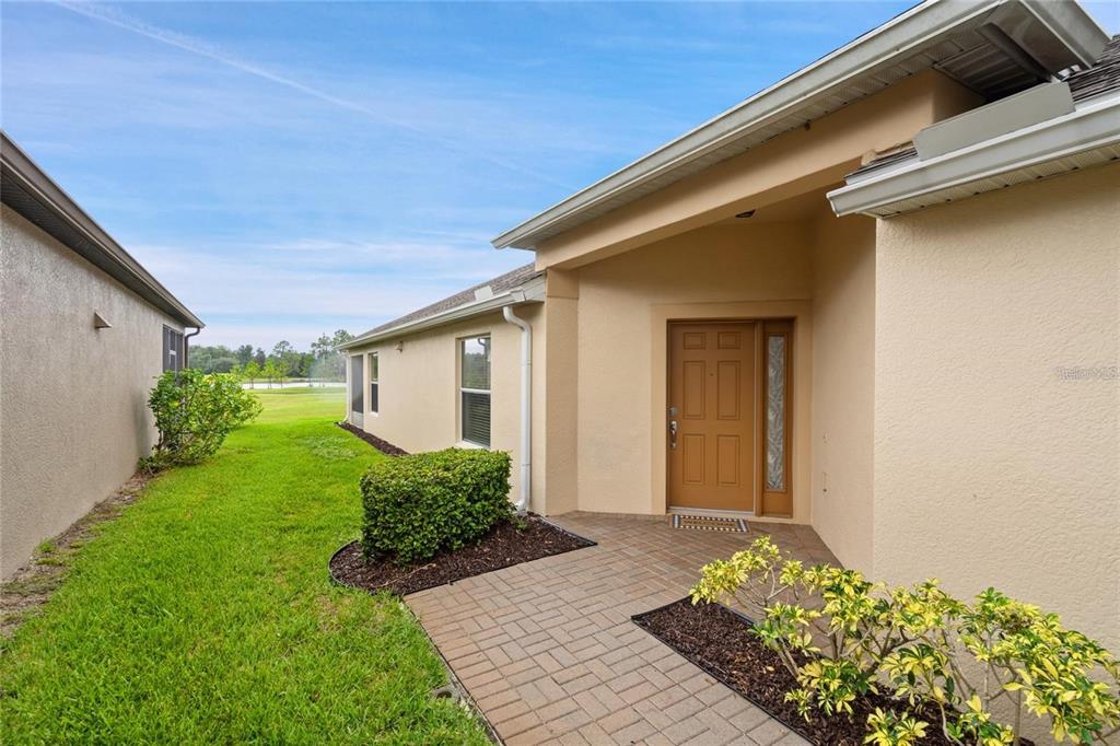 A paved walkway leads to the front entrance of a tan house with a brown door — 418 DEL SOL AVENUE, DAVENPORT, FL