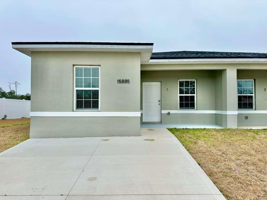A single-story duplex exterior features a concrete driveway, a white front door, and gray siding — 15885 SW 35TH COURT ROAD UNIT 1, OCALA, FL