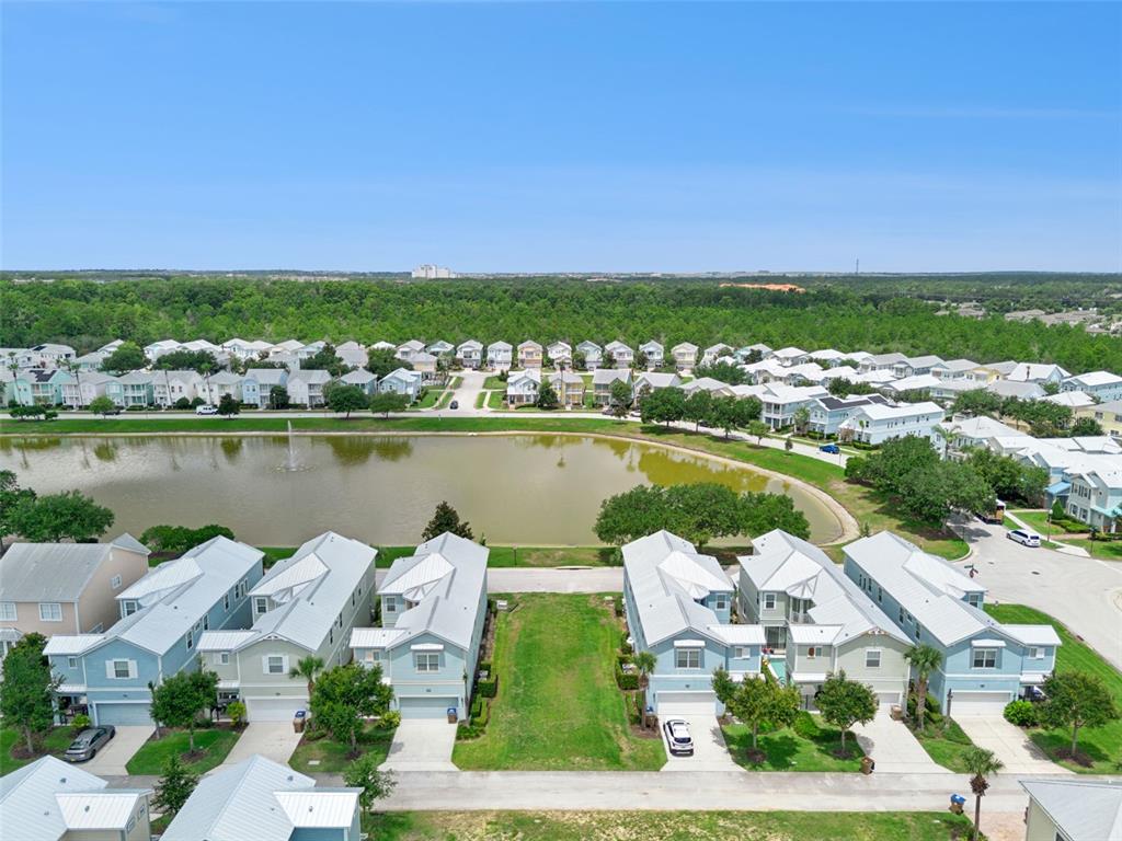 An aerial view shows a row of light-colored townhomes facing a pond and woods — 1513 FAIRVIEW CIRCLE, REUNION, FL
