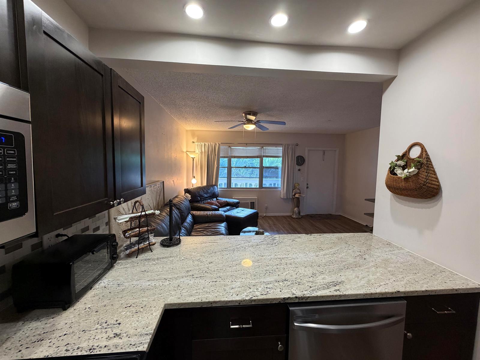 A kitchen with granite countertops overlooks a living room featuring a leather sofa and ceiling fan — 107 Prescott E, Deerfield Beach FL 33442, DEERFIELD BEACH, FL