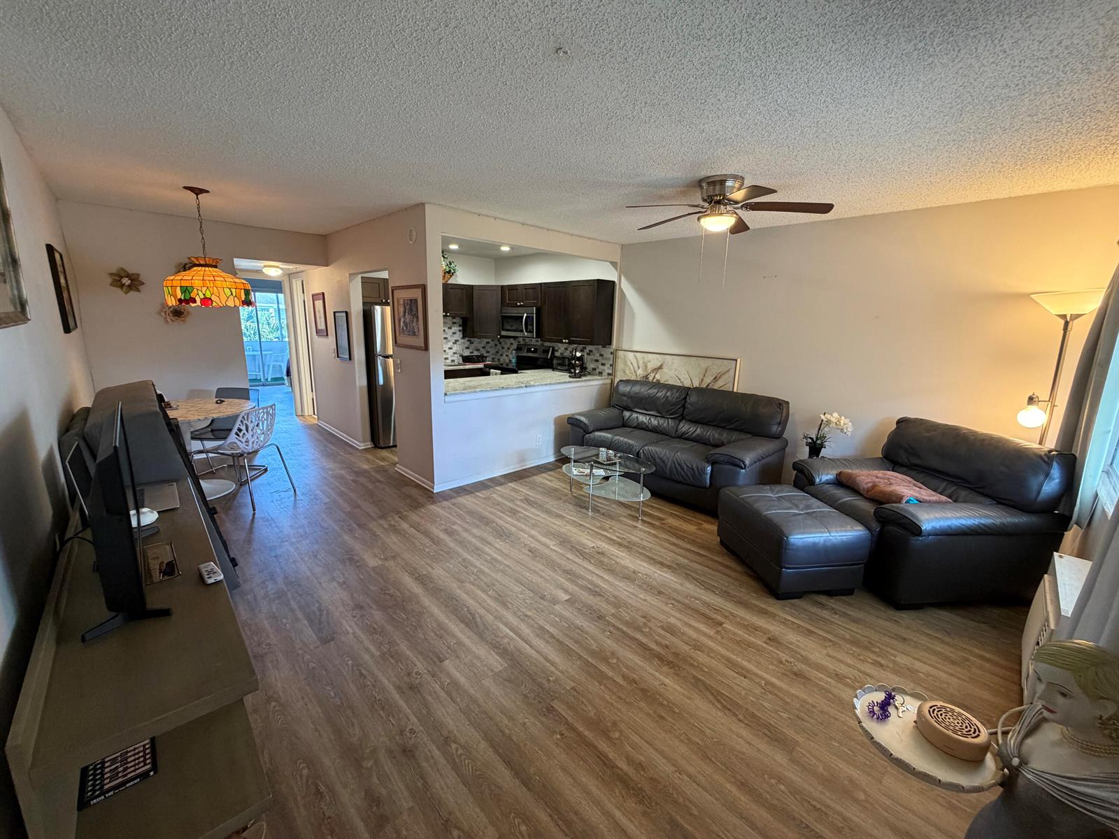 A living room with wood-look flooring, dark leather furniture, and an open kitchen pass-through — 107 Prescott E, Deerfield Beach FL 33442, DEERFIELD BEACH, FL