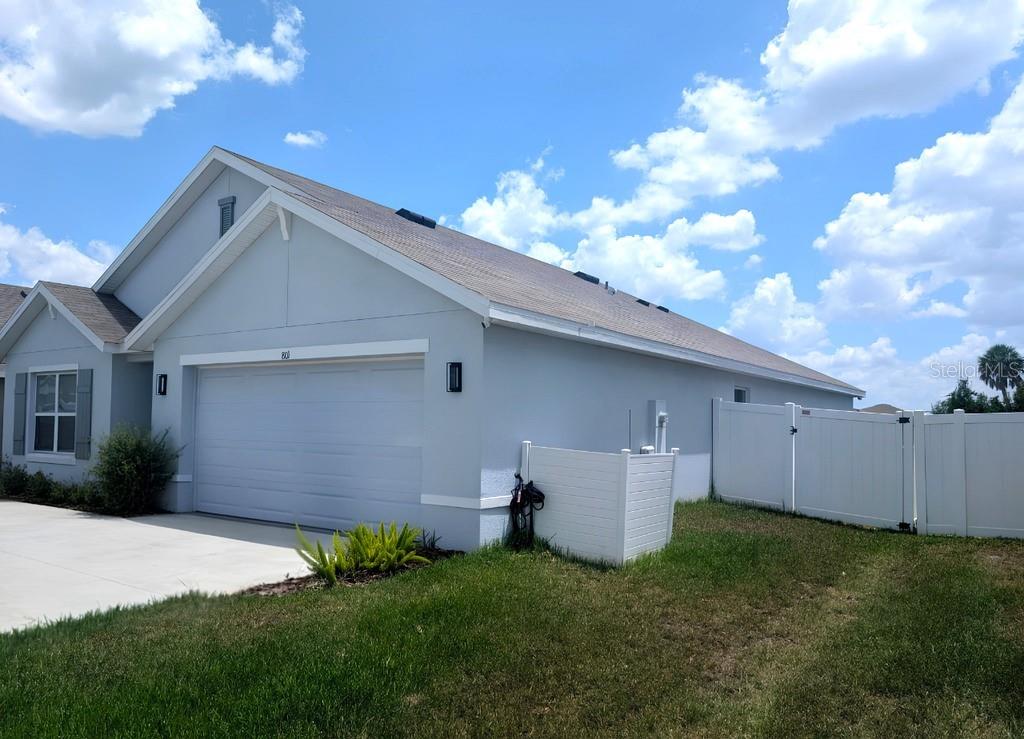 A light gray single-story house features a two-car garage, a concrete driveway, and white fencing — 801 ACE OUTLAW AVENUE, RUSKIN, FL