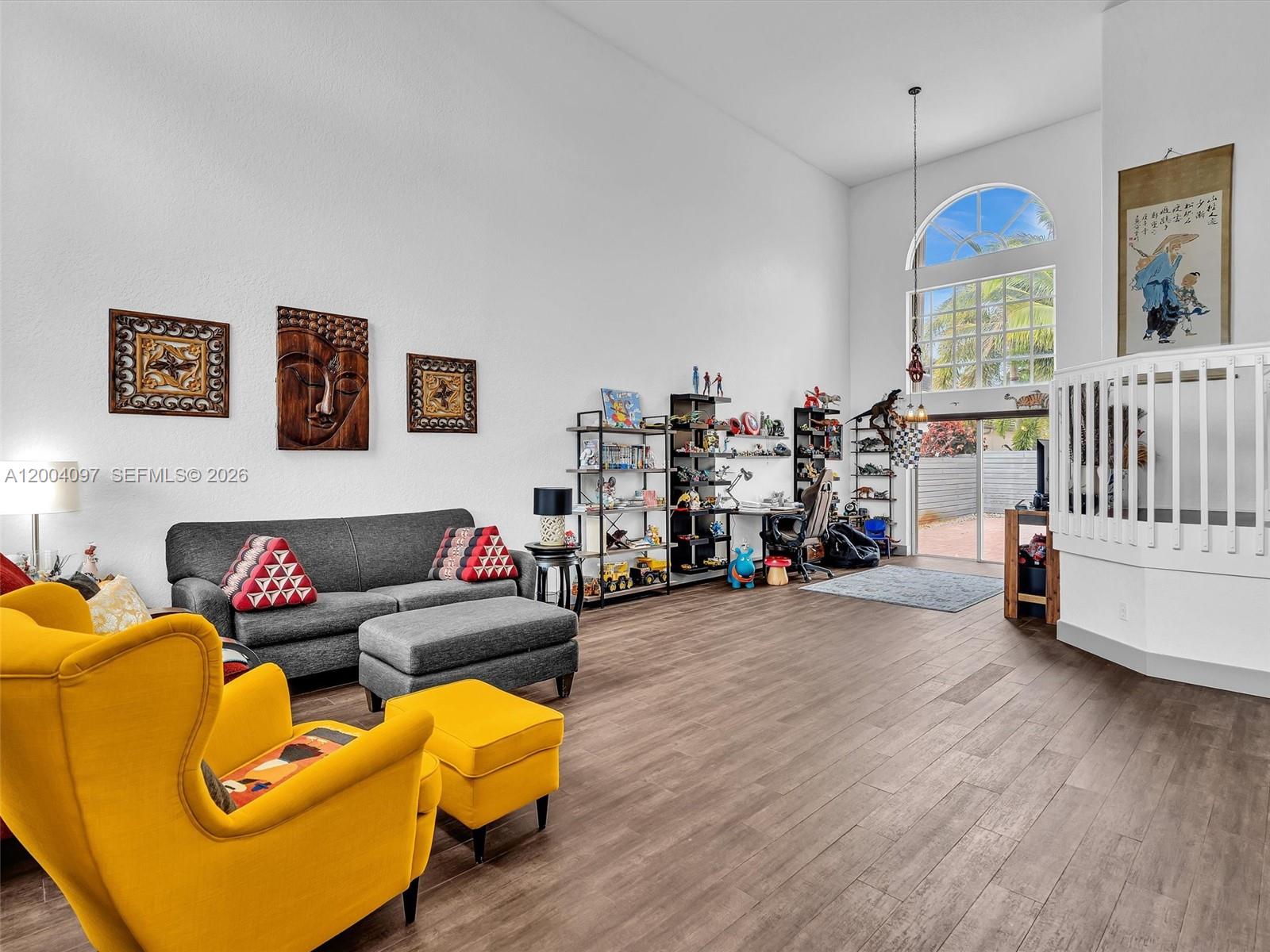 A living room features high ceilings, wood-look flooring, a yellow armchair, and shelving units — 17351 SW 32nd Ct, Miramar FL 33029, MIRAMAR, FL