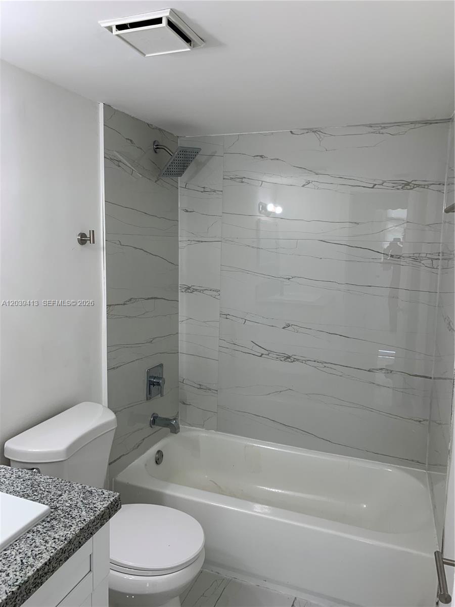 A bathroom features a white bathtub with marble-patterned tile walls and a granite vanity — NORTH MIAMI, FL