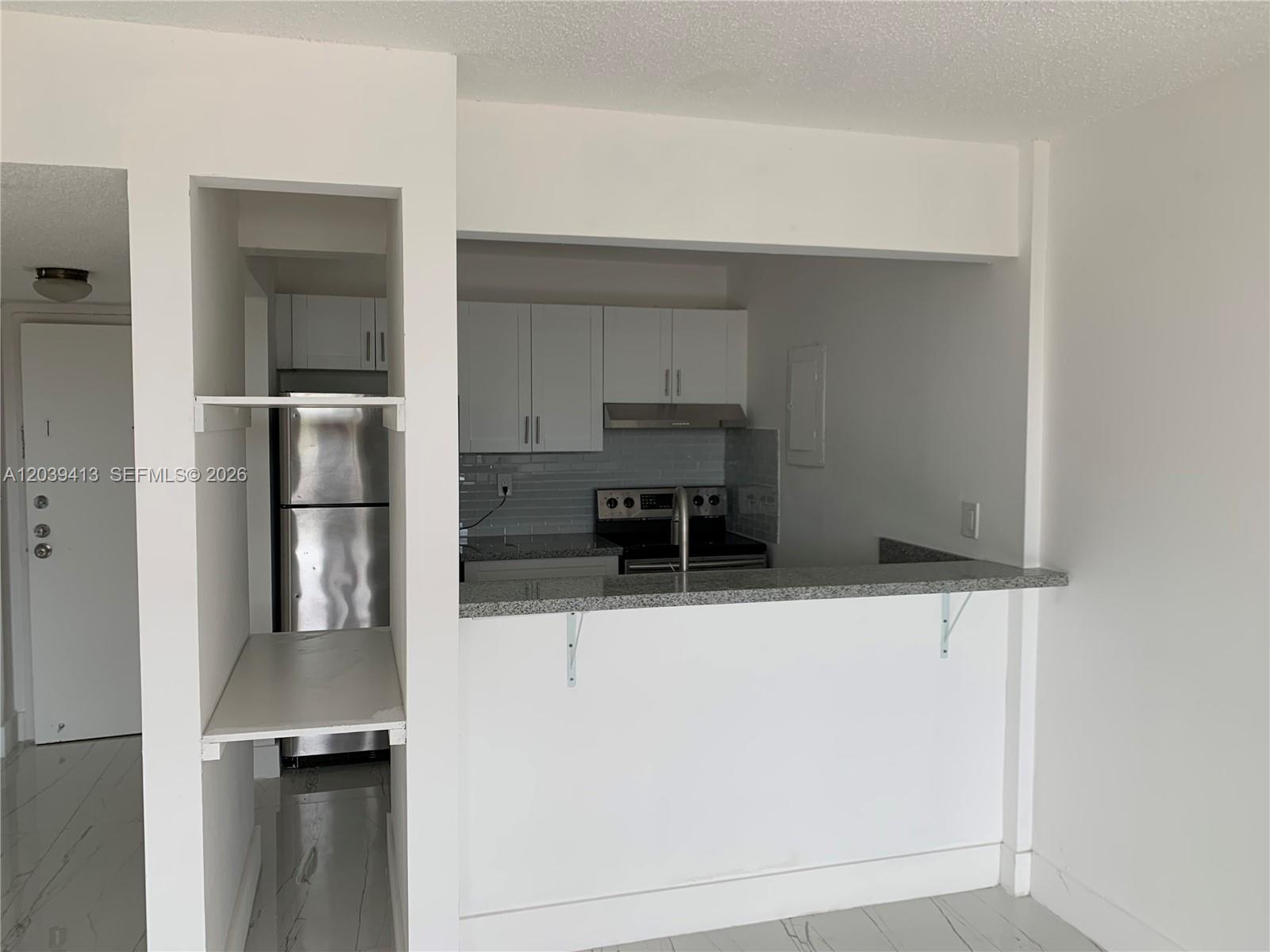 A kitchen features white cabinets, stainless steel appliances, and a granite breakfast bar — NORTH MIAMI, FL