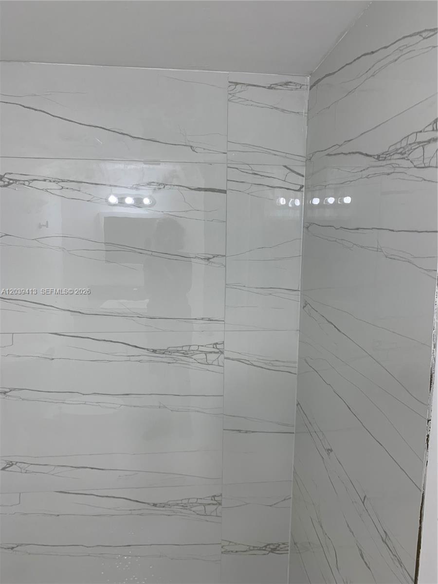 A corner view of a shower wall featuring large white marble-look tiles with grey veining — NORTH MIAMI, FL