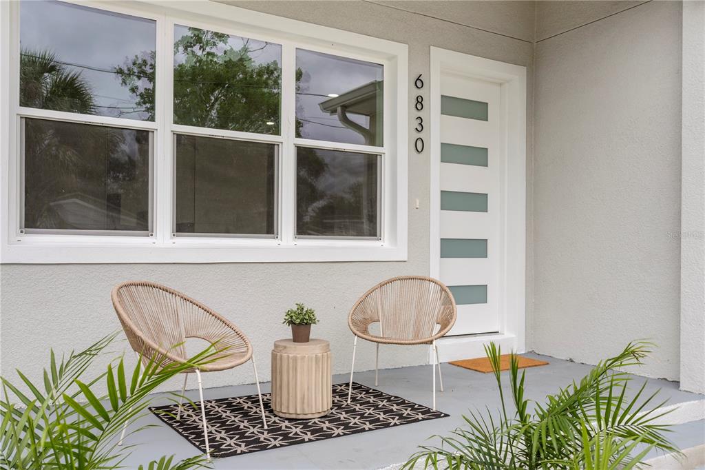 A front porch features two woven chairs, a small side table, and a patterned rug — 6830 S DE SOTO STREET, TAMPA, FL