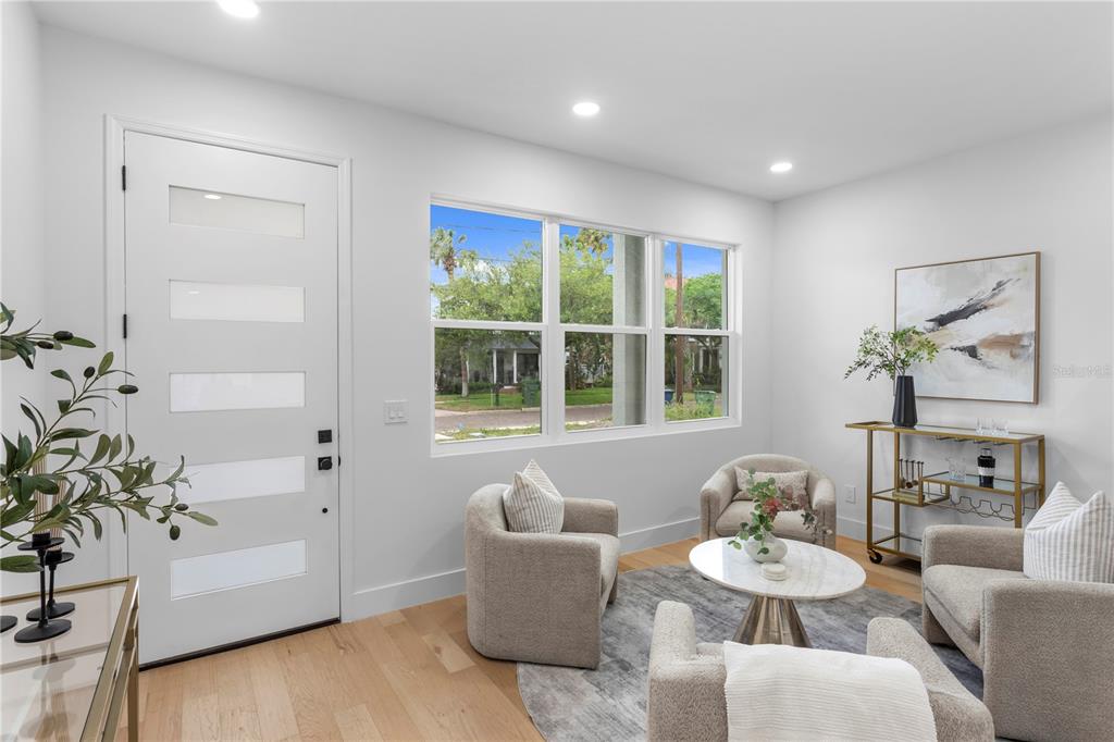 A bright living room features light wood floors, three armchairs, a coffee table, and windows — 6830 S DE SOTO STREET, TAMPA, FL