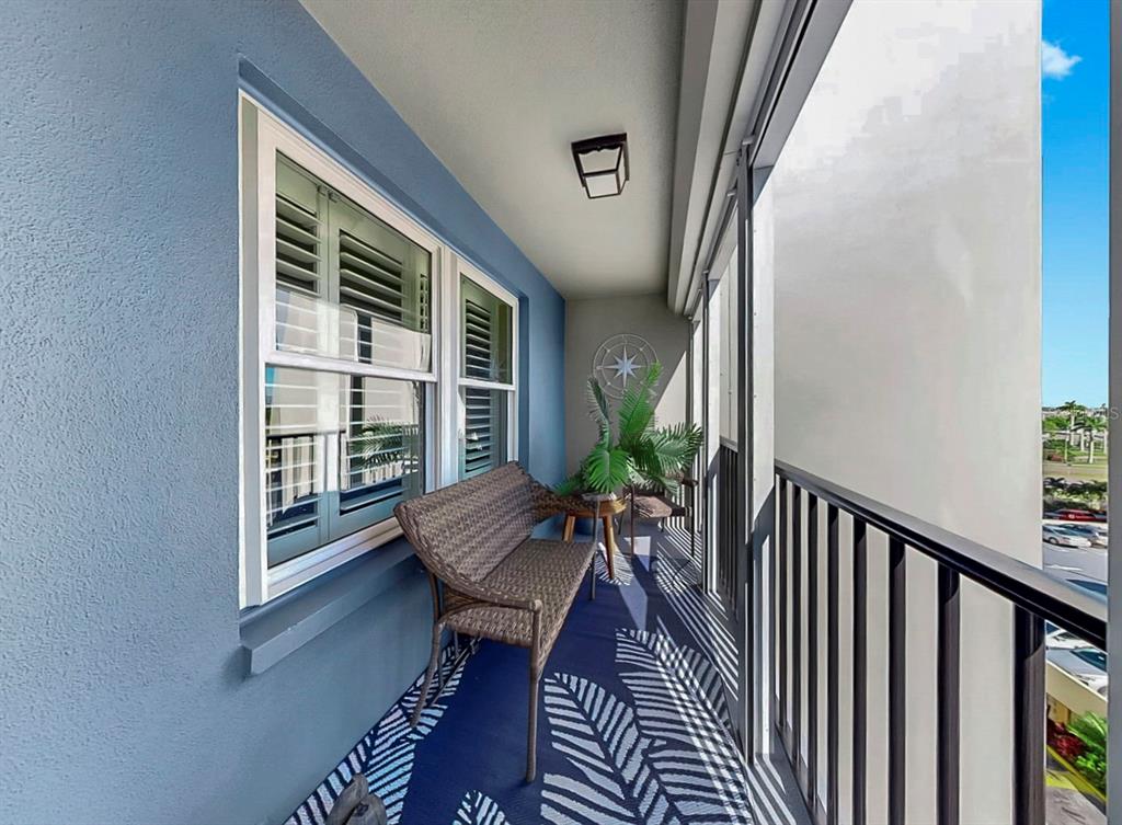 A covered balcony features a wicker bench, a patterned rug, and a black metal railing — 5220 BRITTANY DRIVE S UNIT 603, ST PETERSBURG, FL