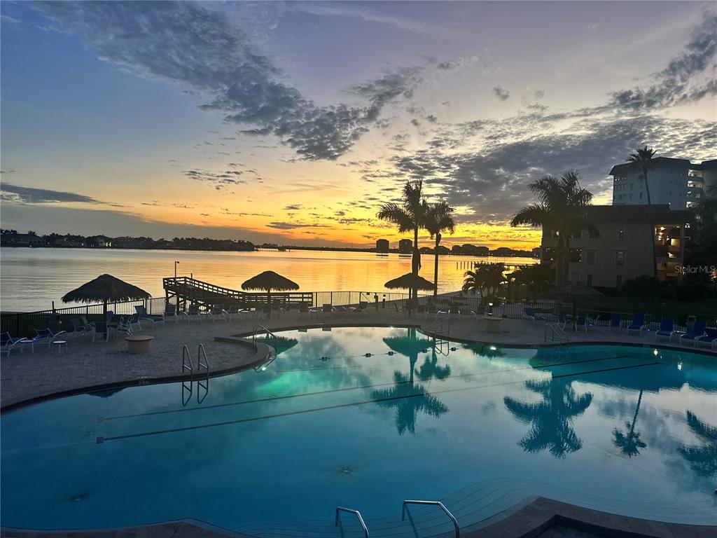 A swimming pool overlooks a waterfront pier and palm trees during a sunset — 5220 BRITTANY DRIVE S UNIT 603, ST PETERSBURG, FL