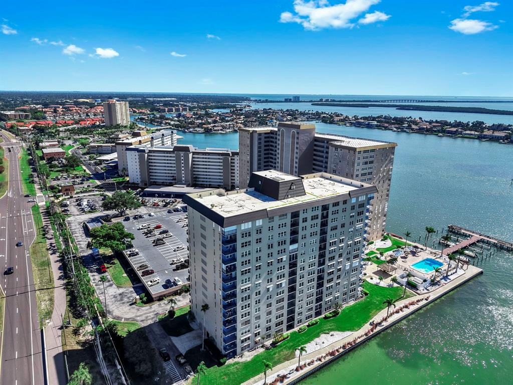An aerial view shows high-rise apartment buildings situated along a waterfront with a swimming pool — 5220 BRITTANY DRIVE S UNIT 603, ST PETERSBURG, FL
