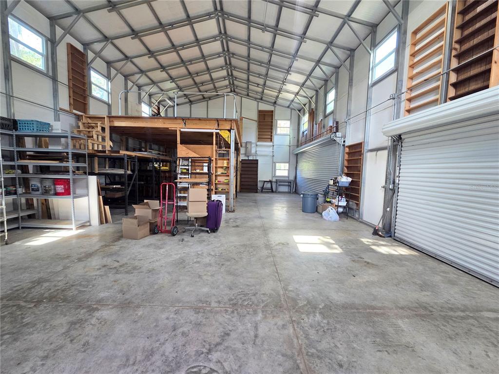 A spacious metal-walled garage features a concrete floor, roll-up door, and wooden loft stairs — 6504 WERNER AVENUE, NEW PORT RICHEY, FL