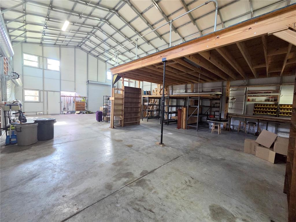 A large metal workshop features a concrete floor, a wooden loft area, and storage shelving — 6504 WERNER AVENUE, NEW PORT RICHEY, FL