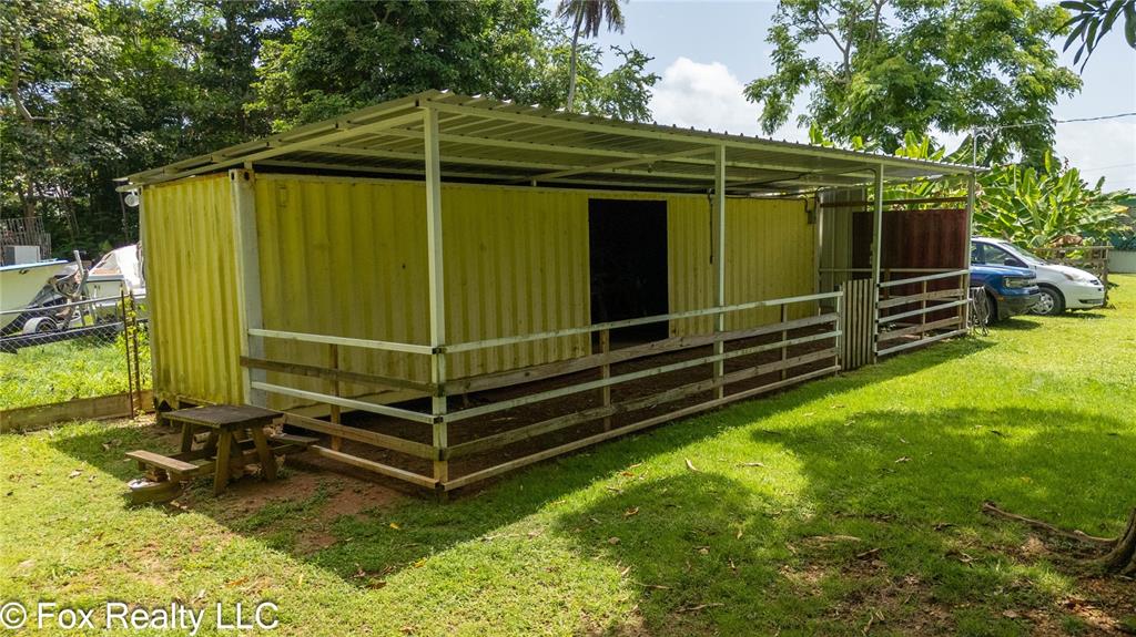 A yellow shipping container structure with a metal roof and fenced enclosure sits on grass — BO ESPINAL, AGUADA, PR