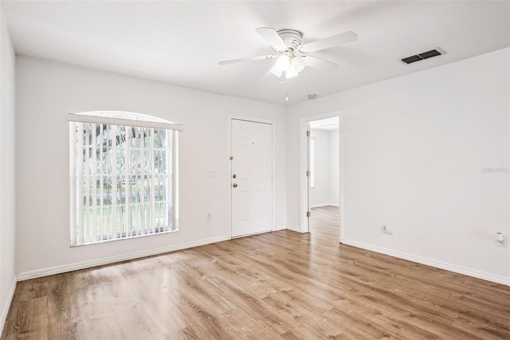 A living room with white walls, wood-look flooring, a ceiling fan, and a front door — 305 E 5TH STREET, ST CLOUD, FL
