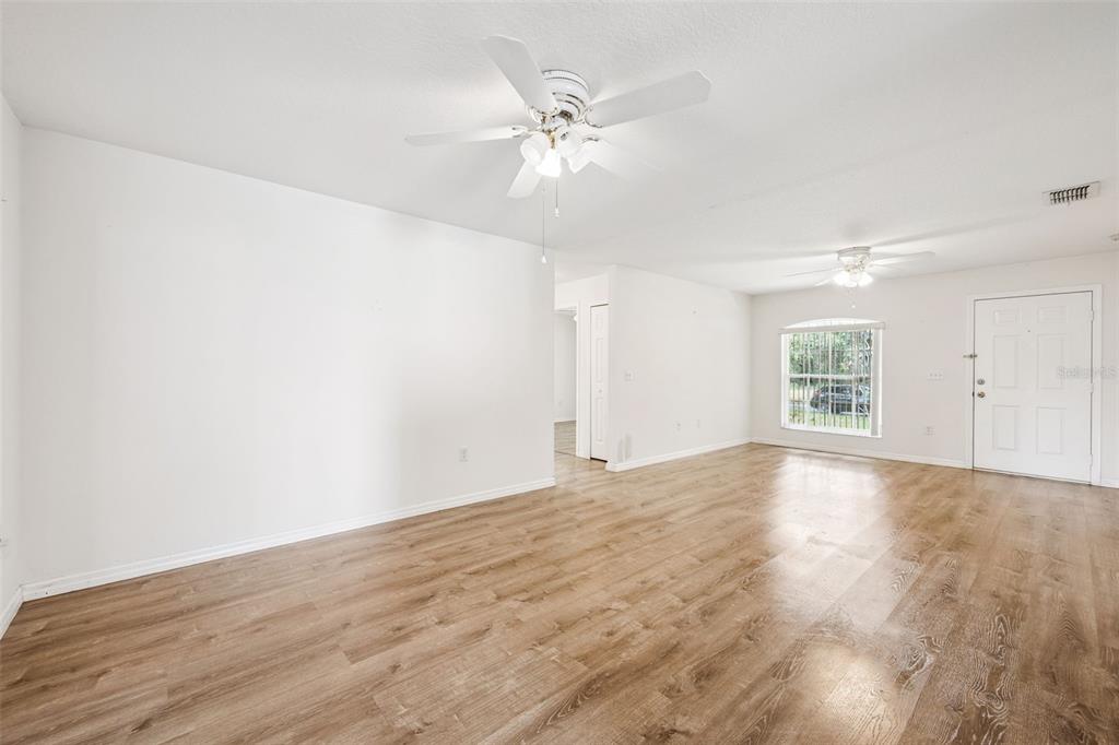An empty living room features light wood-look flooring, white walls, and two ceiling fans — 305 E 5TH STREET, ST CLOUD, FL