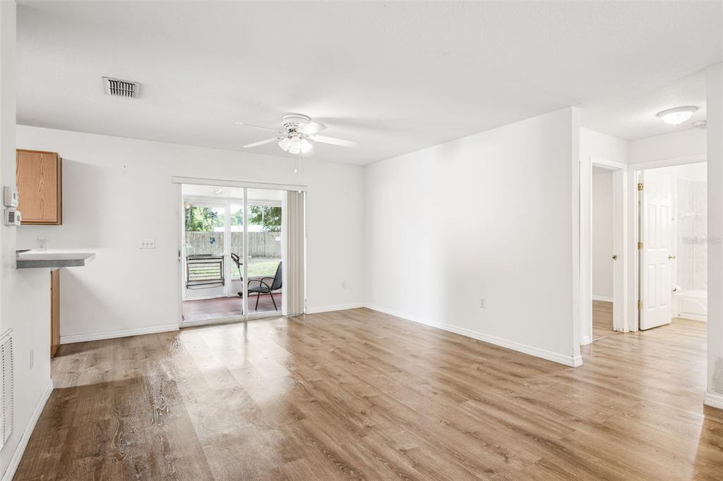 A bright living room features wood-look flooring, a ceiling fan, and sliding glass doors to a patio — 305 E 5TH STREET, ST CLOUD, FL