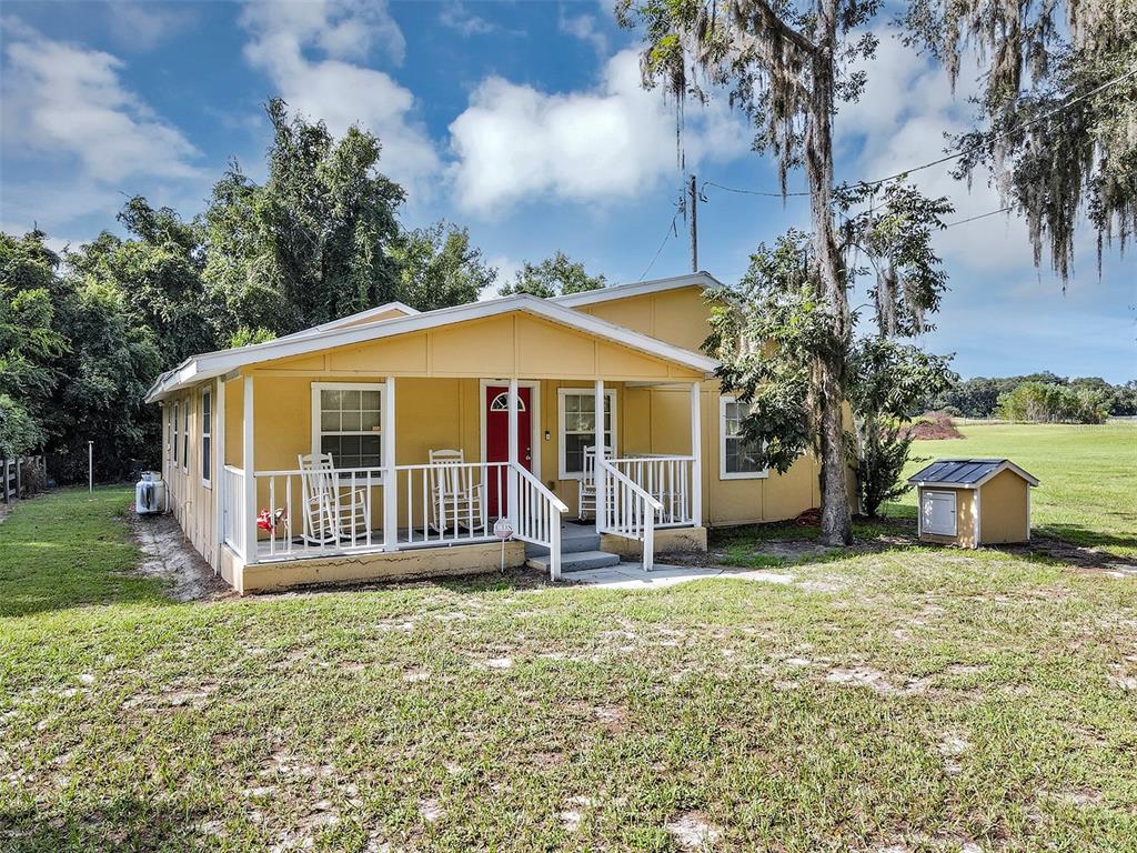 A yellow single-story house features a covered front porch with white railings and a red door — 510 PHILLIPS LANE, WILDWOOD, FL