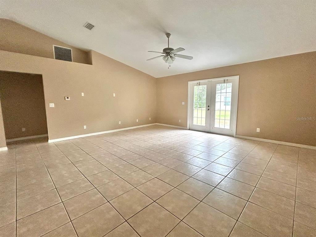 A spacious living room features beige walls, tiled flooring, a vaulted ceiling, and glass doors — 8260 JUNIPER ROAD, OCALA, FL