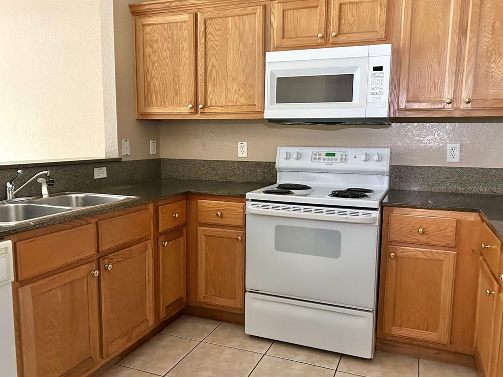 A kitchen with oak cabinets, dark countertops, white appliances, and light-colored tile flooring — 8260 JUNIPER ROAD, OCALA, FL