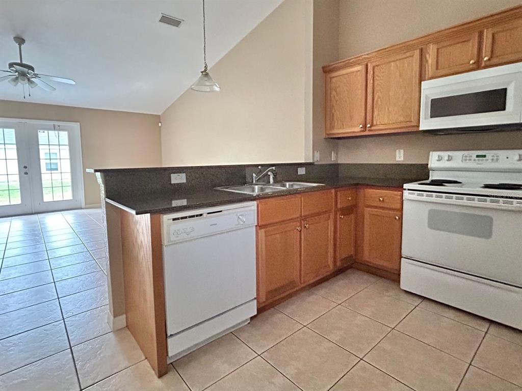 A kitchen features oak cabinets, dark granite countertops, white appliances, and tiled flooring — 8260 JUNIPER ROAD, OCALA, FL
