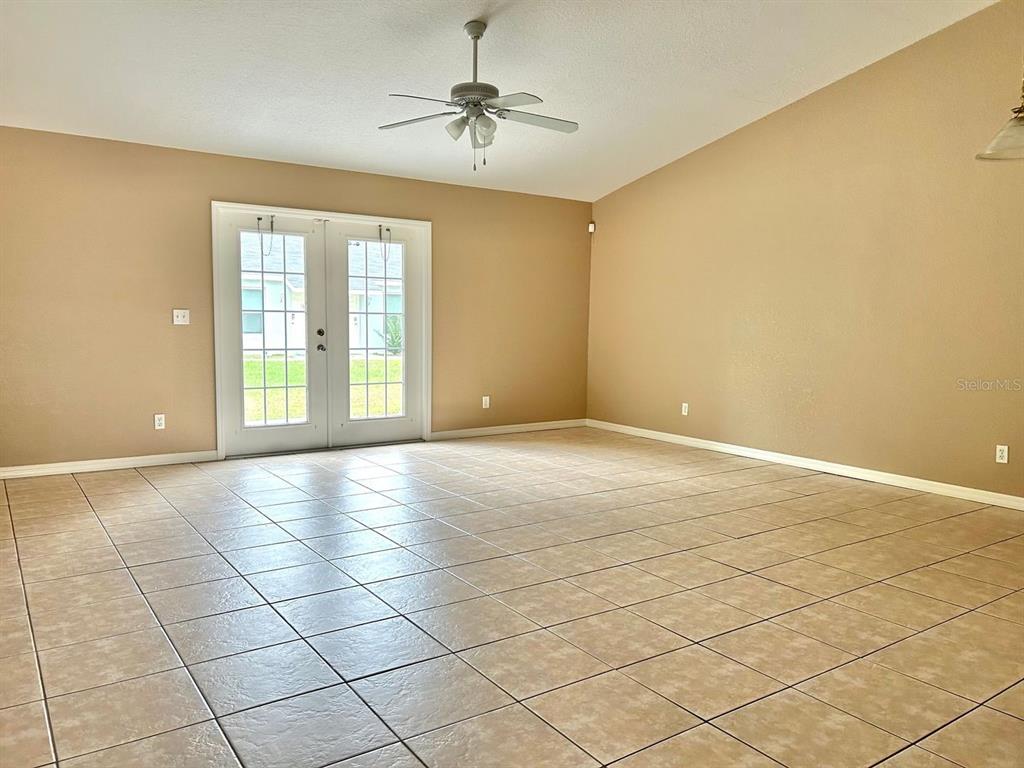 An empty room features tan walls, a ceiling fan, and light-colored tile flooring — 8260 JUNIPER ROAD, OCALA, FL
