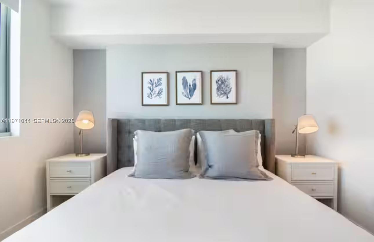 A bedroom features a gray upholstered headboard, two white nightstands with lamps, and three framed prints — 3900 Biscayne Blvd # 402, Miami FL 33137, MIAMI, FL