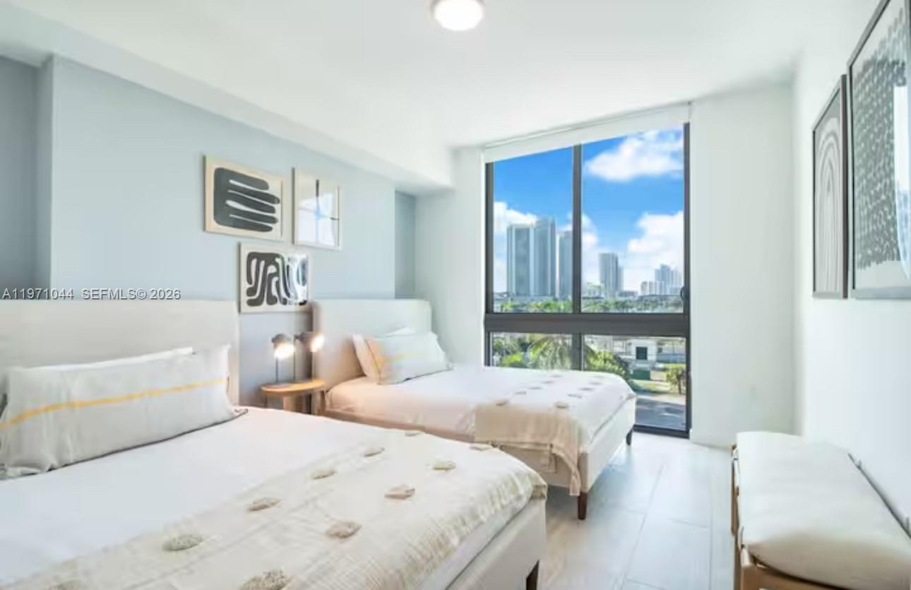 A bedroom features two beds, light blue walls, and a large window with city views — 3900 Biscayne Blvd # 402, Miami FL 33137, MIAMI, FL