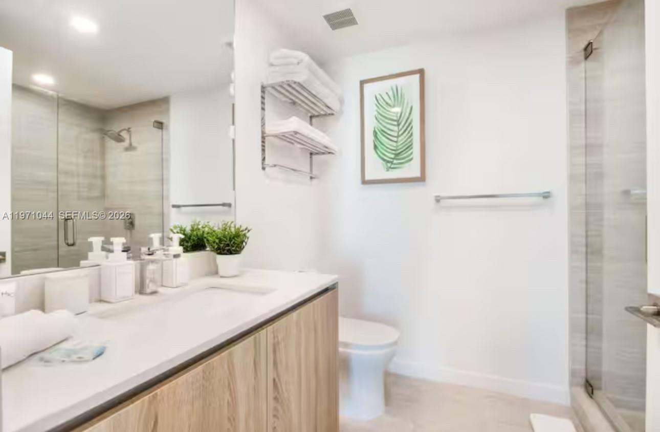 A modern bathroom features a light wood vanity, a glass-enclosed shower, and white walls — 3900 Biscayne Blvd # 402, Miami FL 33137, MIAMI, FL