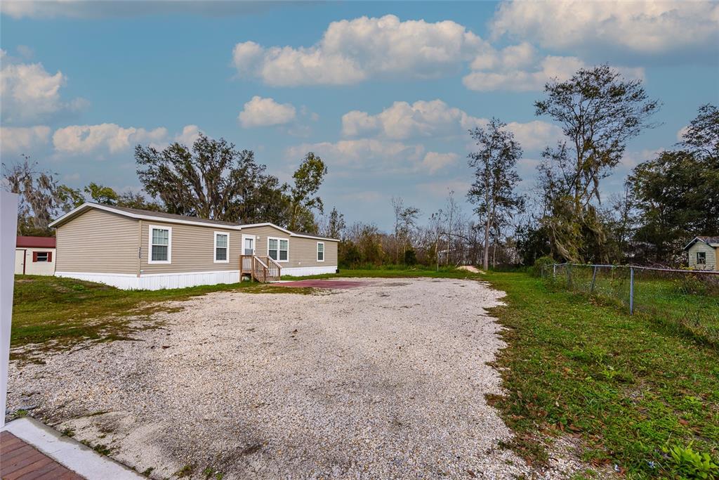 A tan mobile home sits on a gravel lot under a blue sky with clouds — 3205 J AND J MANOR ROAD, LAKELAND, FL