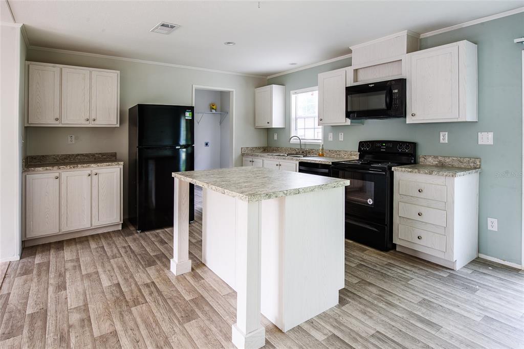 A kitchen features light wood cabinets, black appliances, a central island, and wood-look flooring — 3205 J AND J MANOR ROAD, LAKELAND, FL