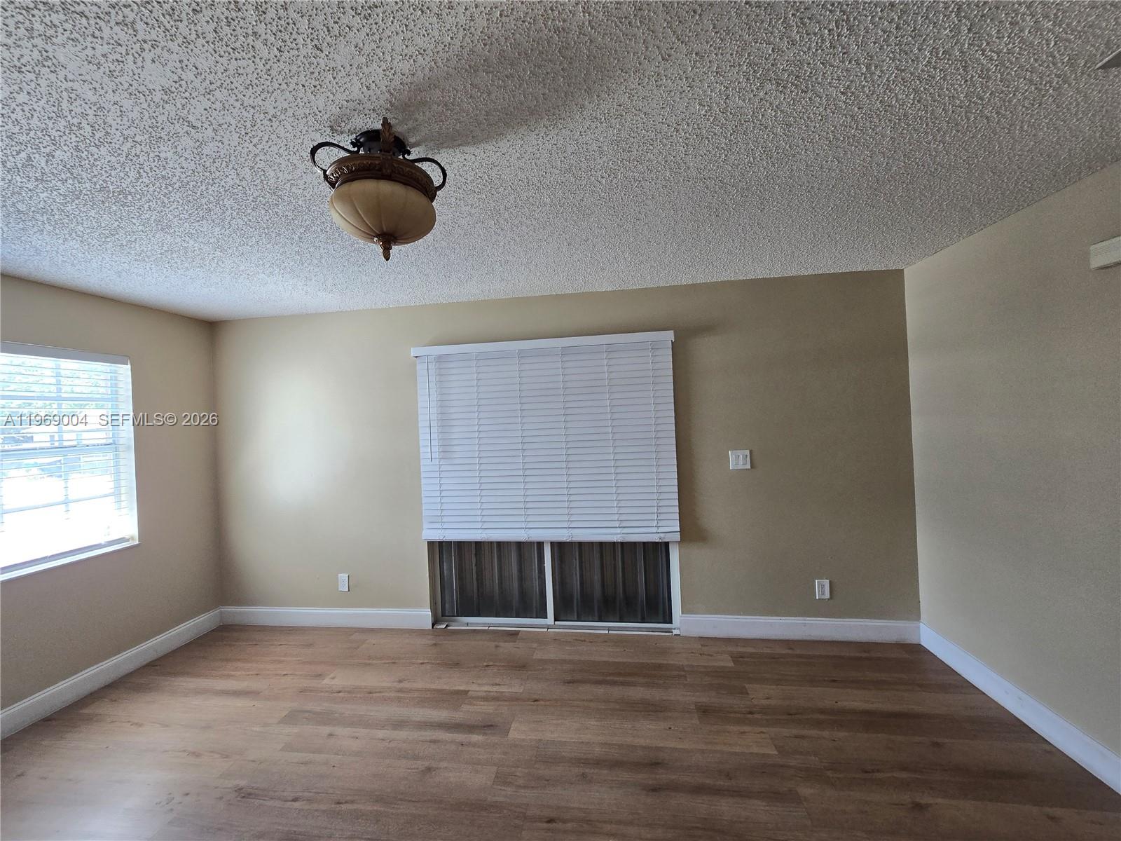 An empty room features wood-look flooring, beige walls, a popcorn ceiling, and a sliding door — 230 NW 7th Ave, Dania Beach FL 33004, DANIA BEACH, FL