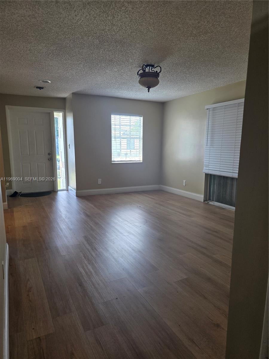 An empty living room features wood-look flooring, a textured ceiling, and a front entrance door — 230 NW 7th Ave, Dania Beach FL 33004, DANIA BEACH, FL