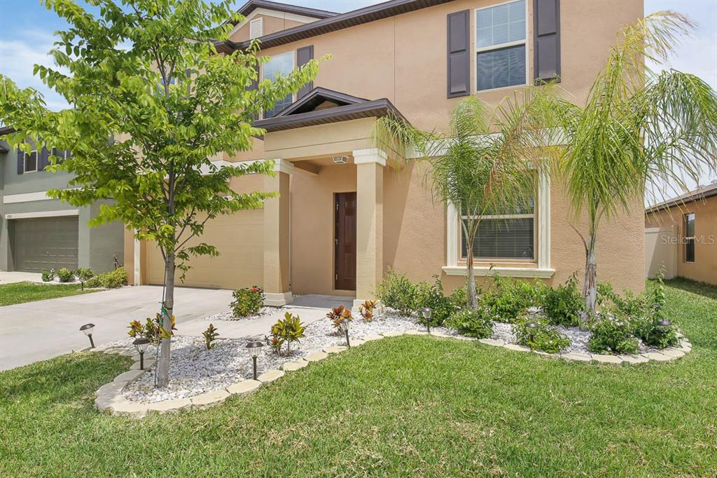 A two-story tan house with a front porch, a driveway, and landscaped garden beds — 7322 KING CREEK DRIVE, SUN CITY CENTER, FL