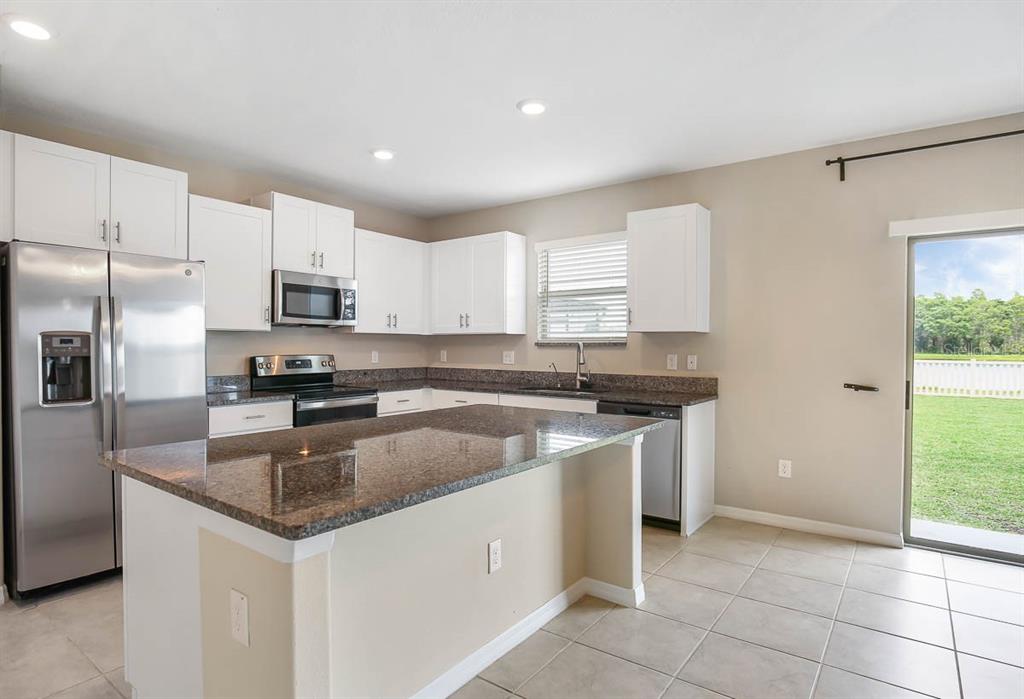 A kitchen features white cabinets, granite countertops, stainless steel appliances, and a central island — 7322 KING CREEK DRIVE, SUN CITY CENTER, FL