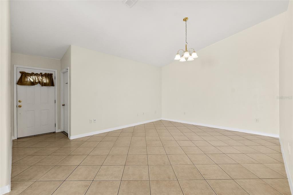 An empty room with beige tile flooring, white walls, and a hanging chandelier — 18 PROSPECT LANE UNIT A & B, PALM COAST, FL