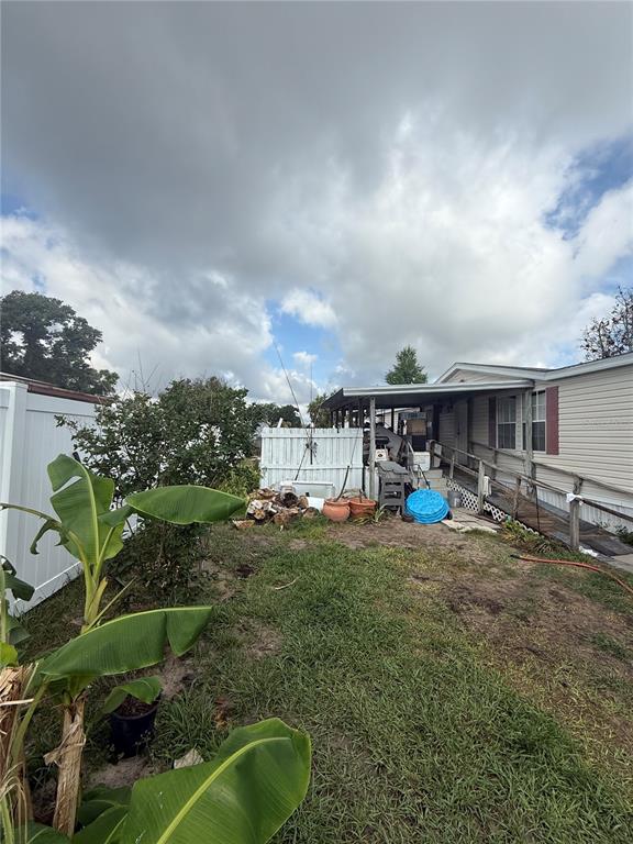 A view of a backyard with a banana plant, a white fence, and a mobile home — 4439 AUTUMN PALM DRIVE, ZEPHYRHILLS, FL