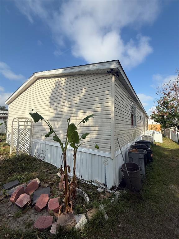 The exterior side of a light-colored mobile home features vinyl siding and a small garden — 4439 AUTUMN PALM DRIVE, ZEPHYRHILLS, FL