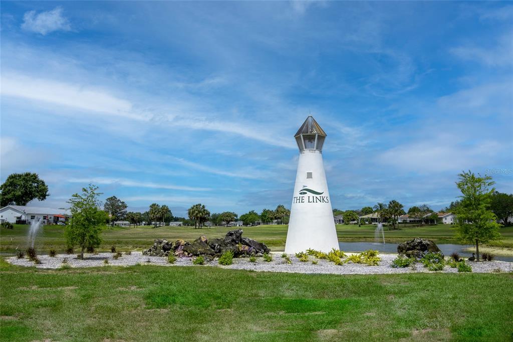 A white lighthouse monument stands on a landscaped island in a golf course pond — 17990 SE 100TH TERRACE, SUMMERFIELD, FL
