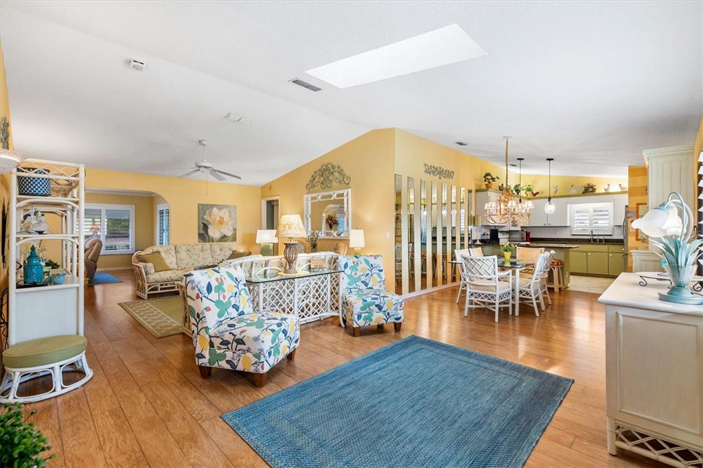 An open-concept living and dining area features yellow walls, hardwood floors, and a skylight — 17990 SE 100TH TERRACE, SUMMERFIELD, FL
