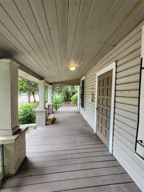 A covered wooden porch features a brown paneled door and white siding — 812 SE 4 AVENUE, GAINESVILLE, FL