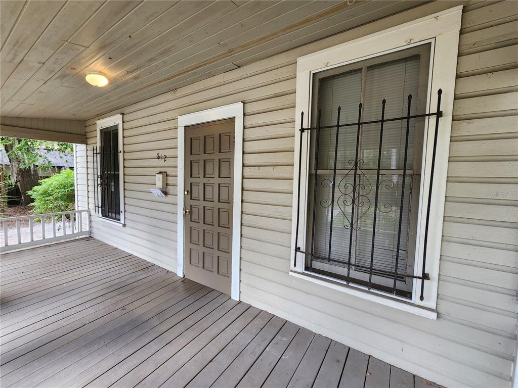 A covered wooden porch features a brown paneled door and two windows with security bars — 812 SE 4 AVENUE, GAINESVILLE, FL