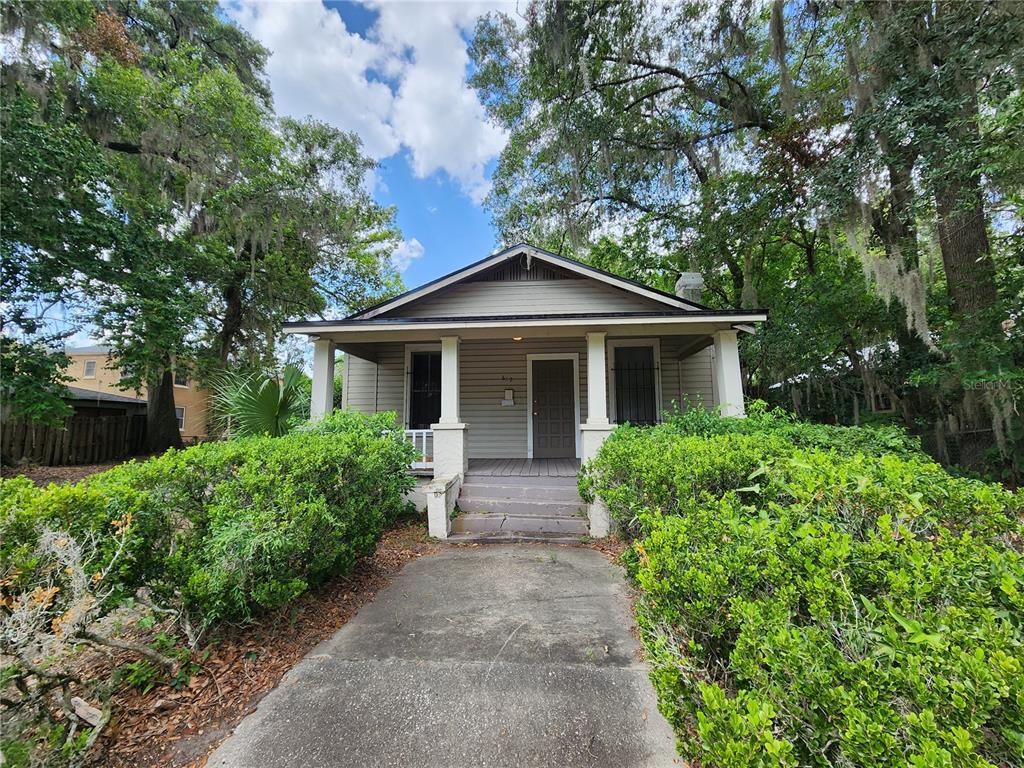 A single-story house with a front porch, concrete walkway, and surrounding trees and shrubs — 812 SE 4 AVENUE, GAINESVILLE, FL